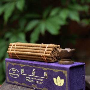 Zestaw kadzideł ajurwedyjskich - grube kadzidła, podstawka i fioletowe opakowanie kadzideł, leżą na stole na tle zieleni