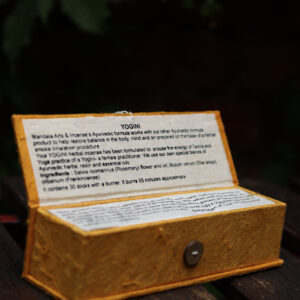 Zestaw kadzideł ajurwedyjskich Yogini - grube kadzidła, podstawka i żółte opakowanie kadzideł, leżą na stole na tle zieleni