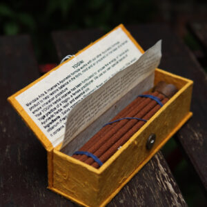 Zestaw kadzideł ajurwedyjskich Yogini - grube kadzidła, podstawka i żółte opakowanie kadzideł, leżą na stole na tle zieleni