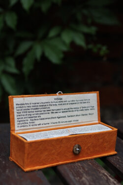 Zestaw kadzideł ajurwedyjskich Yogi - grube kadzidła, podstawka i pomarańczowe opakowanie kadzideł, leżą na stole na tle zieleni