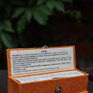 Zestaw kadzideł ajurwedyjskich Yogi - grube kadzidła, podstawka i pomarańczowe opakowanie kadzideł, leżą na stole na tle zieleni