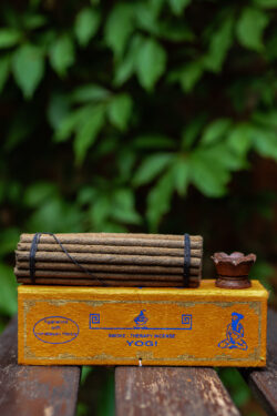 Zestaw kadzideł ajurwedyjskich Yogi - grube kadzidła, podstawka i pomarańczowe opakowanie kadzideł, leżą na stole na tle zieleni