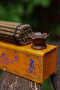 Zestaw kadzideł ajurwedyjskich Yogi - grube kadzidła, podstawka i pomarańczowe opakowanie kadzideł, leżą na stole na tle zieleni