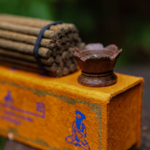 Zestaw kadzideł ajurwedyjskich Yogi - grube kadzidła, podstawka i pomarańczowe opakowanie kadzideł, leżą na stole na tle zieleni