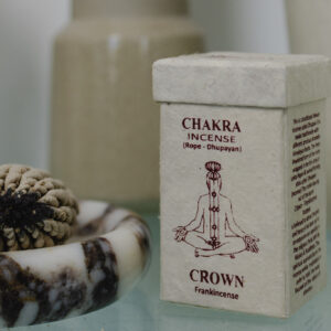 Kadzidełka sznurkowe Chakra Incense na ceramicznej podstawce, obok prostokątne opakowanie na kadzidła z papieru czerpanego na szklanym stole