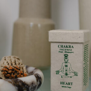 Kadzidełka sznurkowe Chakra Incense na marmurowej podstawce, obok prostokątne opakowanie na kadzidła z papieru czerpanego na szklanym stole