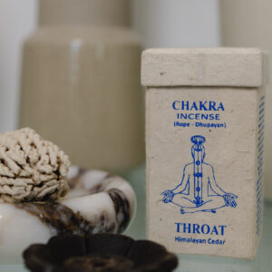 Kadzidełka sznurkowe Chakra Incense na marmurowej podstawce, obok prostokątne opakowanie na kadzidła z papieru czerpanego na szklanym stole