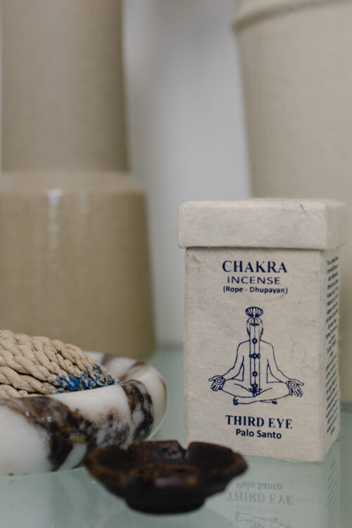 Kadzidła Chakra Third Eye Kadzidełka sznurkowe Chakra Incense na marmurowej podstawce, obok prostokątne opakowanie na kadzidła z papieru czerpanego na szklanym stole