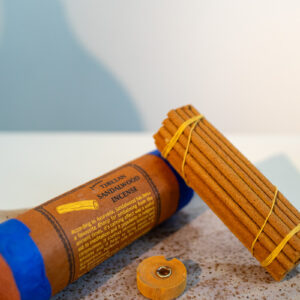 Grube kadzidła tybetańskie Tibetan Sandalwood oparte o tubę z papieru czerpanego, w zestawie z podstawką; kadzidła leżą na ceramicznej tacy na bialym tle