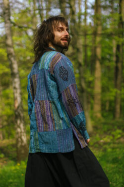 Mężczyzna w długich włosach w patchworkowej koszuli z długim rękawem na tle drzew