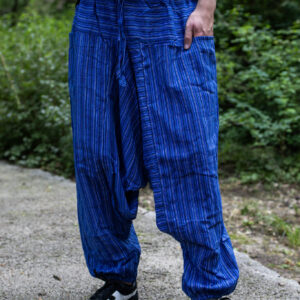 Mężczyzna w czarnej koszuli i niebieskich szarawarach w paski stojący na ścieżce w parku