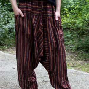 Mężczyzna w czarnej koszuli i bordowo-czerwonych szarawarach w paski stojący na ścieżce w parku