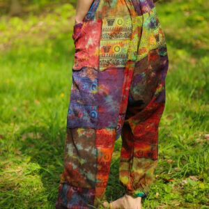 Kobieta w tęczowych szarawarach patchwork i czarnym topie stoi boso w parku