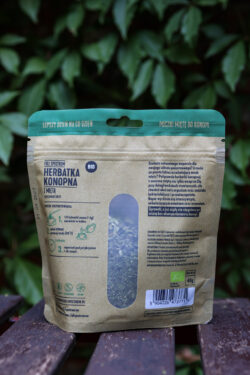 Opakowanie herbatki konopnej BIO z miętą stoi na drewnianym stoliku na tle zieleni.