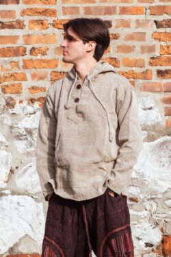 Mężczyzna ubrany w brązowe spodnie baggy i beżową bluzę w jodełkę, stoi na tle ceglanego muru