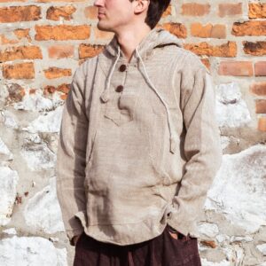 Mężczyzna ubrany w brązowe spodnie baggy i beżową bluzę w jodełkę, stoi na tle ceglanego muru