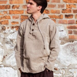 Mężczyzna ubrany w brązowe spodnie baggy i beżową bluzę w jodełkę, stoi na tle ceglanego muru