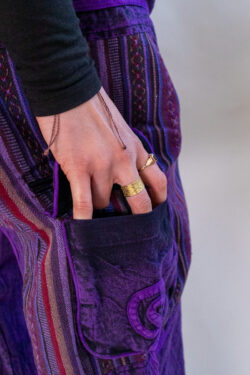 Kobieta w rozpuszczonych, kręconych włosach w czarnej bluzce i fioletowych baggy spodniach w vintage stylu z etnicznymi wzorami i kieszonkami po bokach.