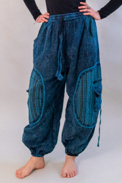 Kobieta w czarnej bluzce i niebieskich baggy spodniach na białym tle. Spodnie przecierane, z kieszonkami po bokach i etniczną bawełną gheri.