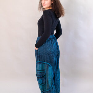 Kobieta w czarnej bluzce i niebieskich baggy spodniach na białym tle. Spodnie przecierane, z kieszonkami po bokach i etniczną bawełną gheri.