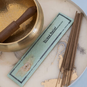 Kadzidelka Stress Relief w niebieskim opakowaniu leżące na marmurowej tacy obok misy dźwiękowej.