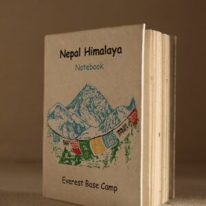 Mały beżowy notes z papieru czerpanego z Himalajami i tybetańskami flagami modlitewnymi na okładce na jasnym tle