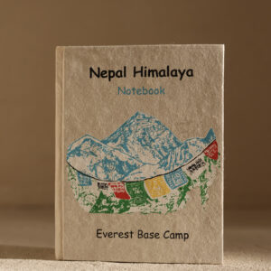 Mały beżowy notes z papieru czerpanego z Himalajami i tybetańskami flagami modlitewnymi na okładce na jasnym tle