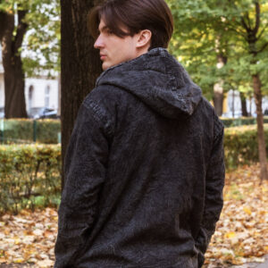 Mężczyzna w szarej kurtce w psychodeliczne wzory z vintage efektem przeciernaia z kapturem na tle zieleni