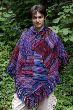 Mężczyzna w trójkątnym, patchworkowym ponczo w fioletowym kolorze na tle zieleni