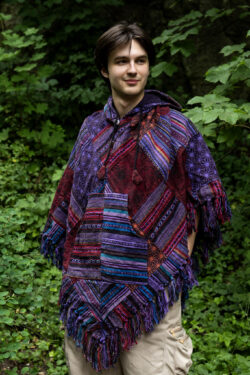 Mężczyzna w trójkątnym, patchworkowym ponczo w fioletowym kolorze na tle zieleni