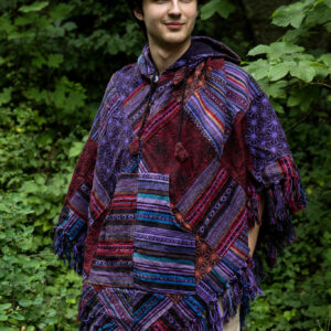 Mężczyzna w trójkątnym, patchworkowym ponczo w fioletowym kolorze na tle zieleni