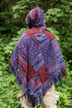 Osoba w trójkątnym, patchworkowym ponczo w fioletowym kolorze na tle zieleni