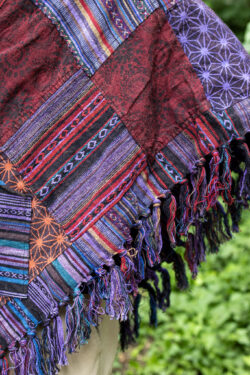 Mężczyzna w trójkątnym, patchworkowym ponczo w fioletowym kolorze na tle zieleni