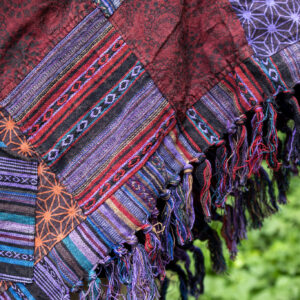 Mężczyzna w trójkątnym, patchworkowym ponczo w fioletowym kolorze na tle zieleni