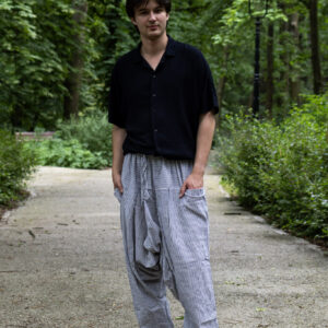 Mężczyzna w czarnej koszuli i białych szarawarach w czarne paski stojący na ścieżce w parku