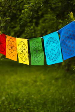 Kolorowa materiałowa girlanda z symbolami Świętej Geometrii rozwieszona wśród drzew.