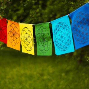 Kolorowa materiałowa girlanda z symbolami Świętej Geometrii rozwieszona wśród drzew.