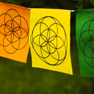 Kolorowa materiałowa girlanda z symbolami Świętej Geometrii rozwieszona wśród drzew.