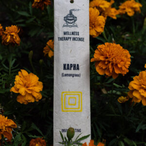 Opakowanie kadzideł Kapha leżące wśród kwiatów.