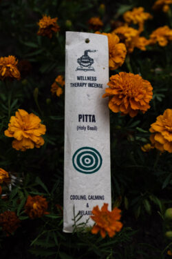 Opakowanie kadzideł Pitta leżące wśród kwiatów.