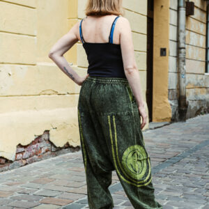 Kobieta w zielonych szarawarach i czarnym topie na ramiączkach stoi tyłem na ulicy