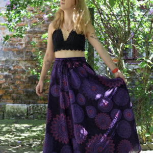 Kobieta w blond włosach i czarnym szydełkowym topie w fioletowej maxi spódnicy w mandale na tle zieleni