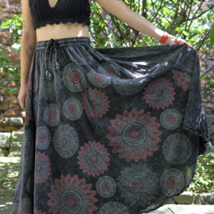 Kobieta w blond włosach i czarnym szydełkowym topie w szarej maxi spódnicy w mandale na tle zieleni