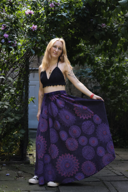 Spódnica w mandale Kobieta w blond włosach i czarnym szydełkowym topie w fioletowej maxi spódnicy w mandale na tle zieleni