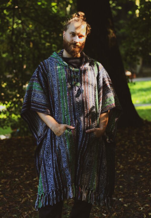 Zielone ponczo Mężczyzna w dlugim brązowo-zielonym ponczo w etno wzory z kapturem stoi na tle zieleni