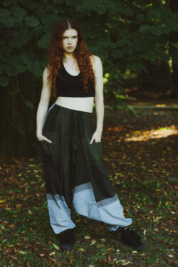 Kobieta z długimi rudymi włosami ubrana w czarny top i zielono-szare szarawary w geometryczne wzory