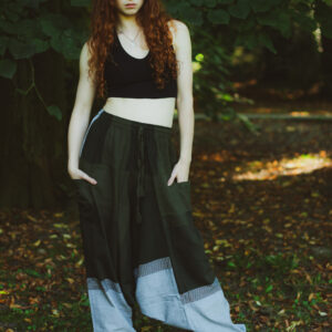 Kobieta z długimi rudymi włosami ubrana w czarny top i zielono-szare szarawary w geometryczne wzory