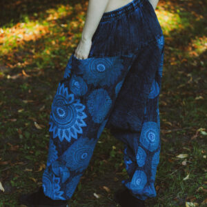 Kobieta w czarnym topie i niebieskich szarawarach ze wzorem mandali stoi na tle zieleni