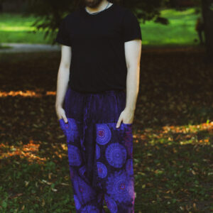 Mężczyzna w czarnym topie i fioletowych szarawarach ze wzorem mandali stoi na tle zieleni