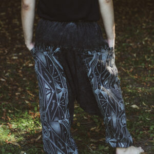 Mężczyzna w szarych alladynkach stoi tyłem boso na trawie